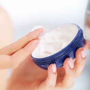 Young woman applying natural cream onto skin at home
